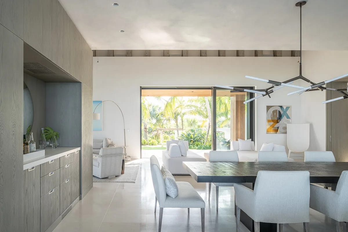 Dining room with rectangular table, white chairs, sideboard, and sliding glass doors to garden view
