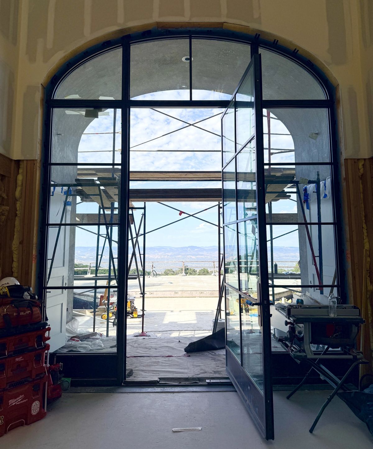 Entryway with large glass doors opening to an outdoor view and construction materials along the walls.