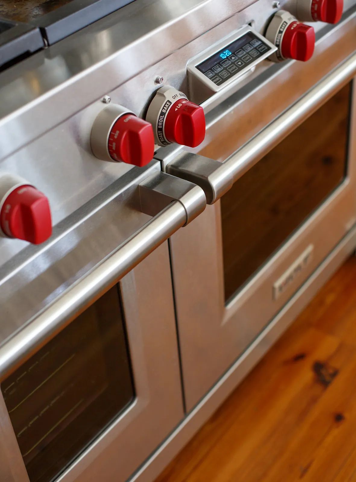 Kitchen with stainless steel oven range featuring red knobs and wooden flooring.