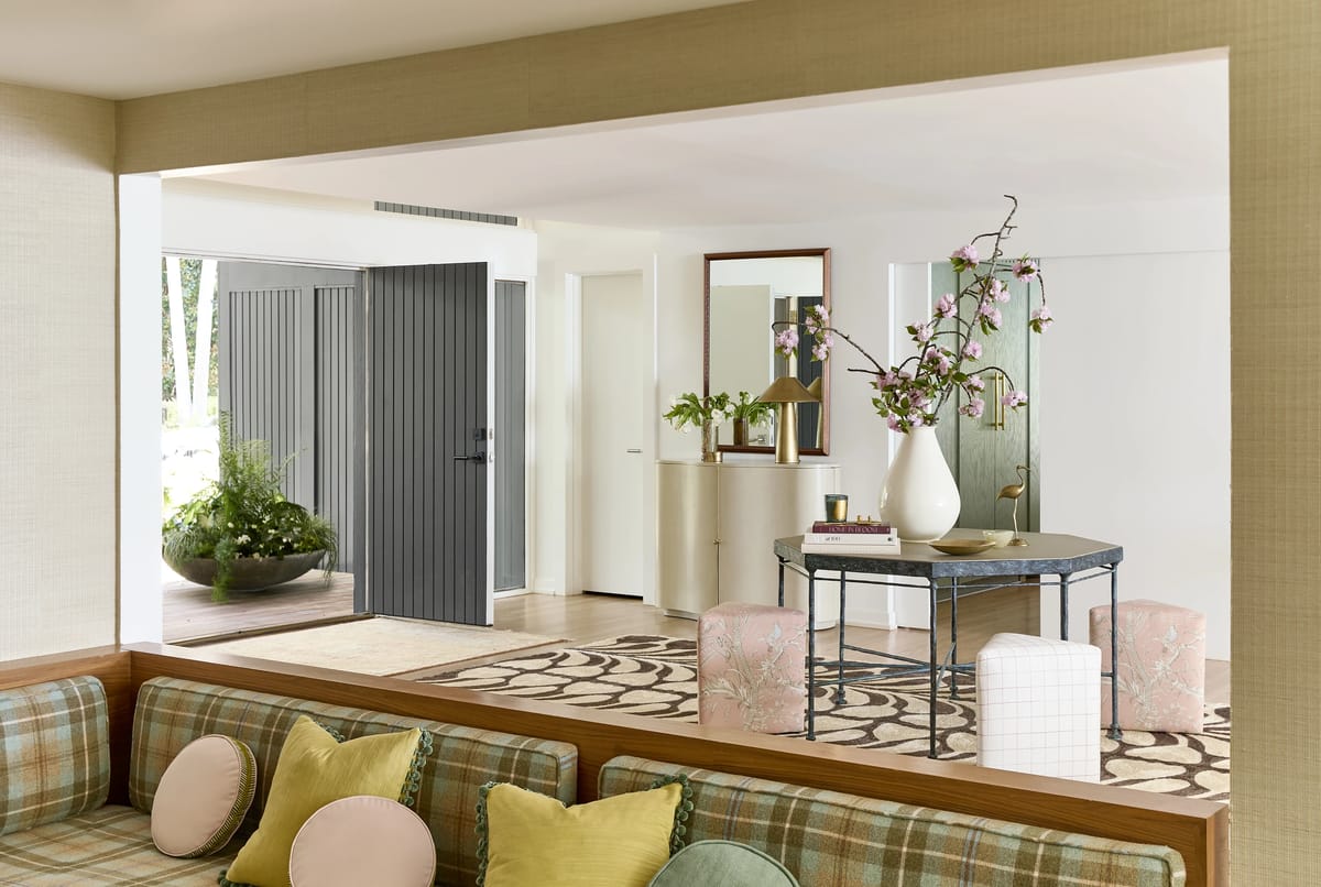 Foyer with gray front door, round table, floral arrangement, mirror, and patterned rug.