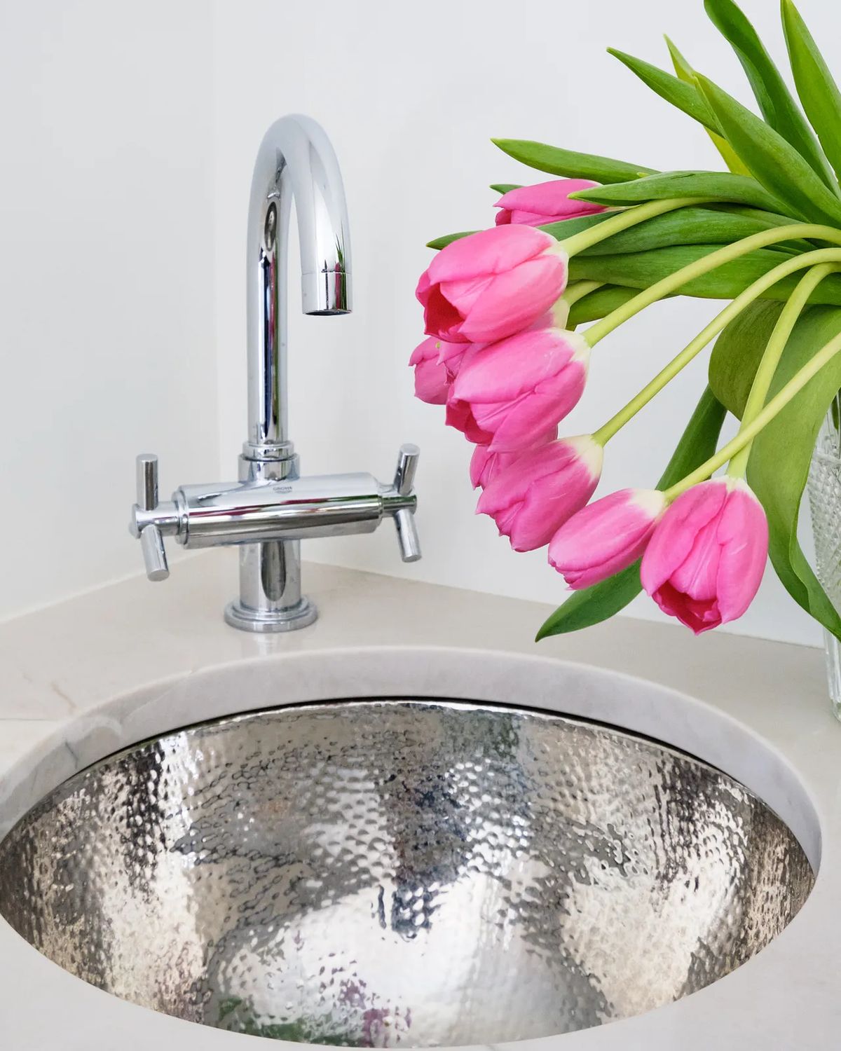 Powder room with polished metal sink, chrome faucet, and bouquet of pink tulips in clear vase