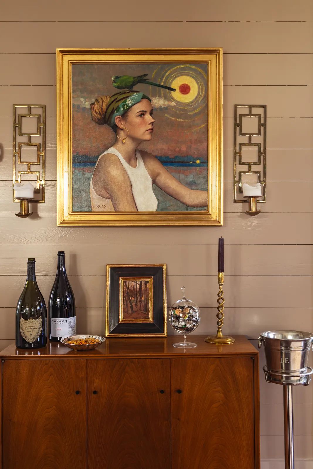 Dining room with wooden sideboard, wine bottles, framed artwork, candle holder, and wall sconces