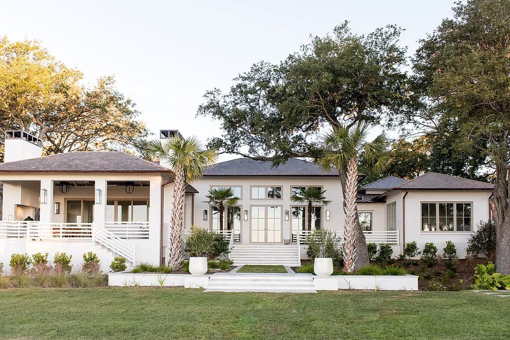 Home exterior with double doors, planters, palm trees, stone pathway, and manicured grass.