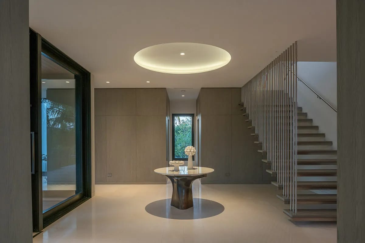 Foyer featuring a round table, decorative object, large windows, wooden staircase, and circular ceiling light.