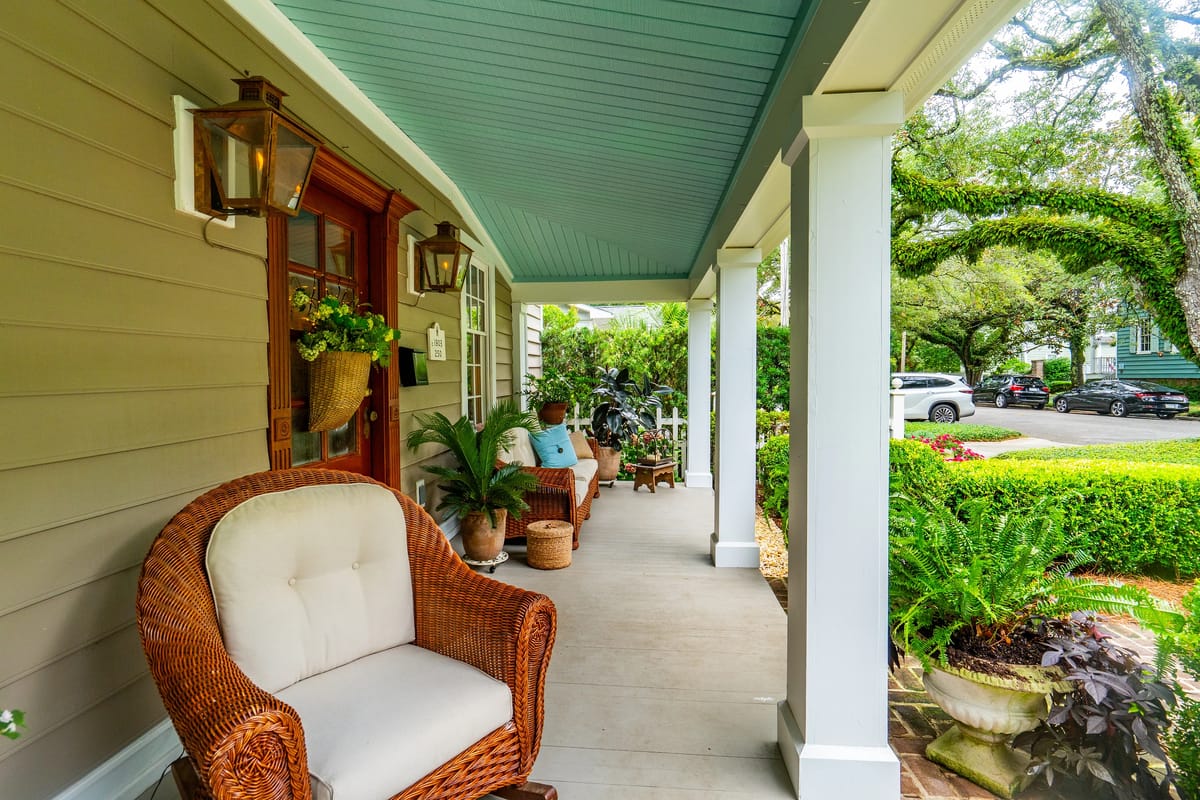 Exterior front porch with wicker chair, potted plants, blue ceiling, and wooden walls.