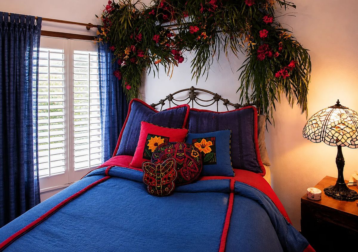 Bedroom with red and blue bedding, decorative pillows, nightstand, floral decor, and stained glass lamp.