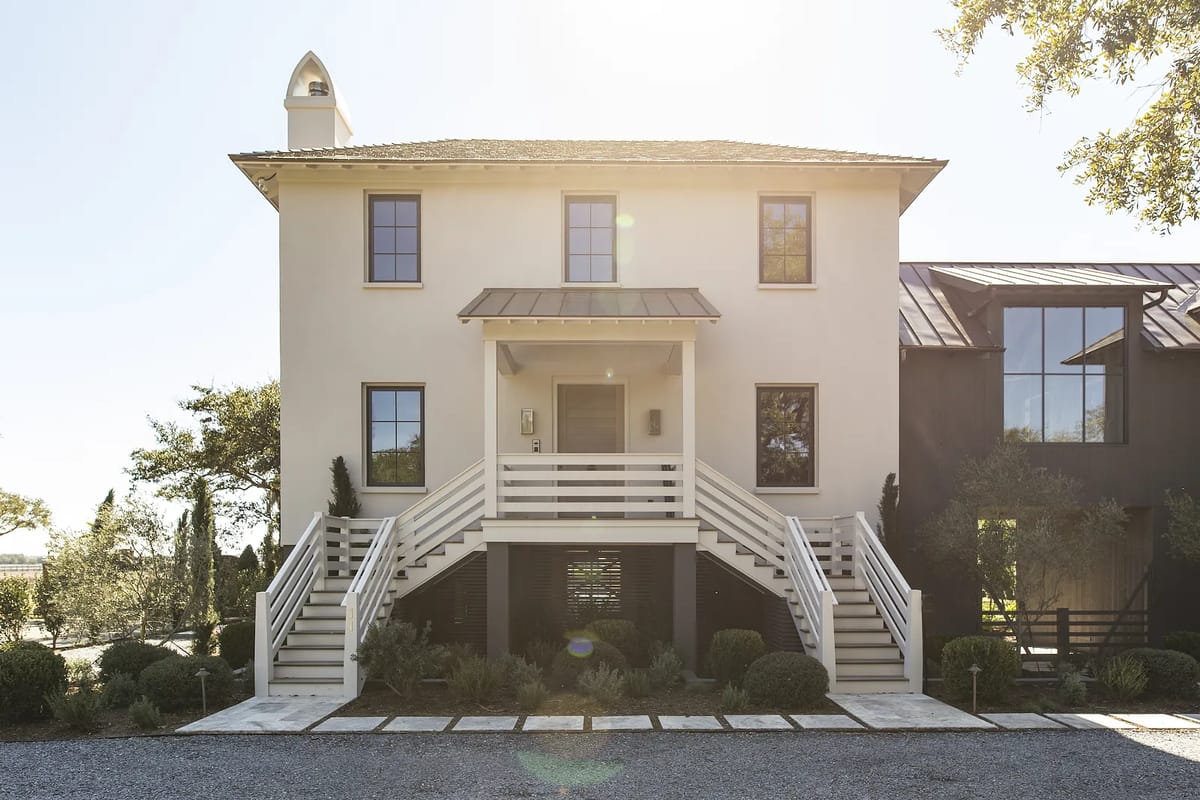 Two-story house exterior with white facade, steps, large windows, chimney, and landscaped front yard.