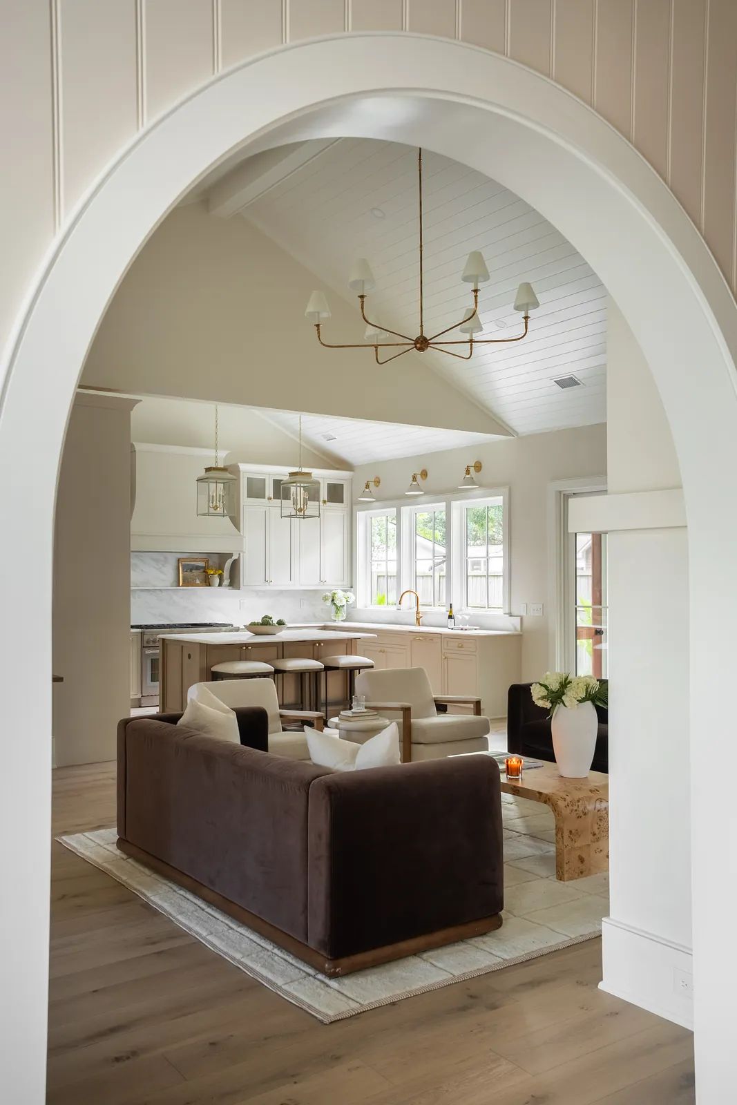 Living room with brown sofa, area rug, round table, dining area, large windows, and white beamed ceiling