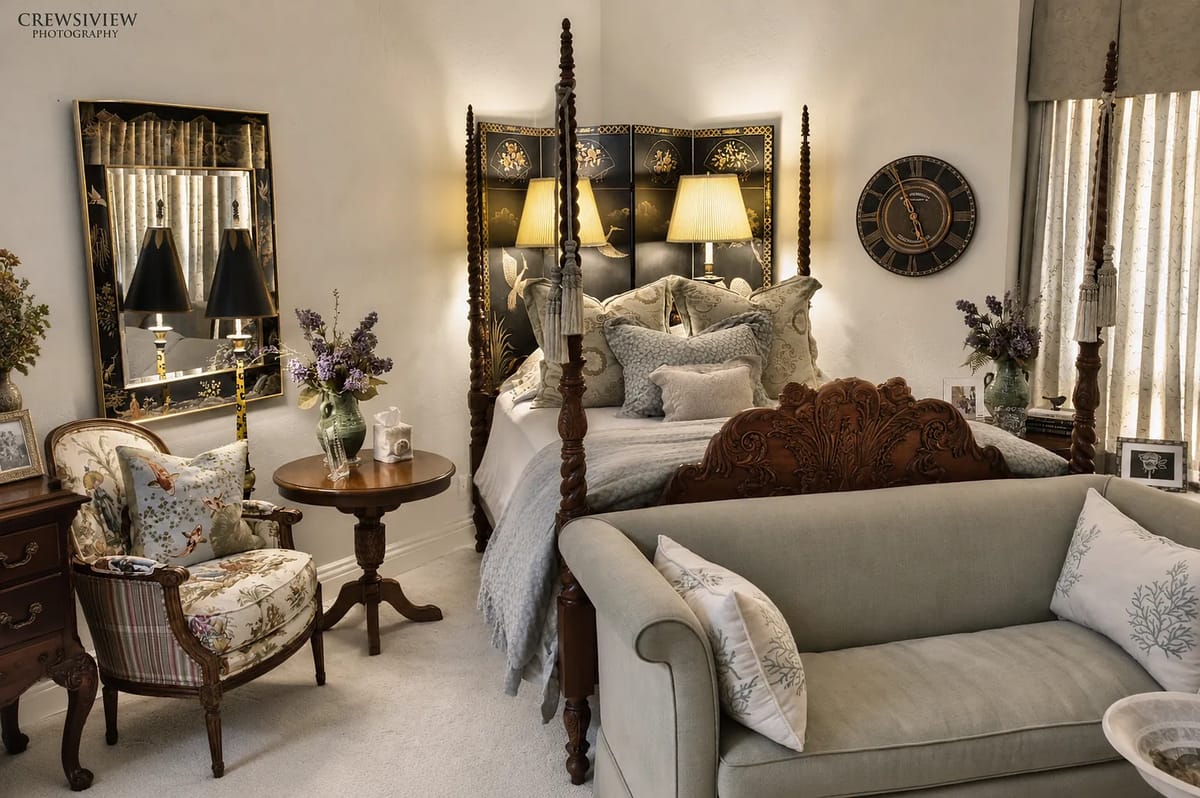 Bedroom with four-poster bed, lamps, sofa, round table, and decorative mirror.