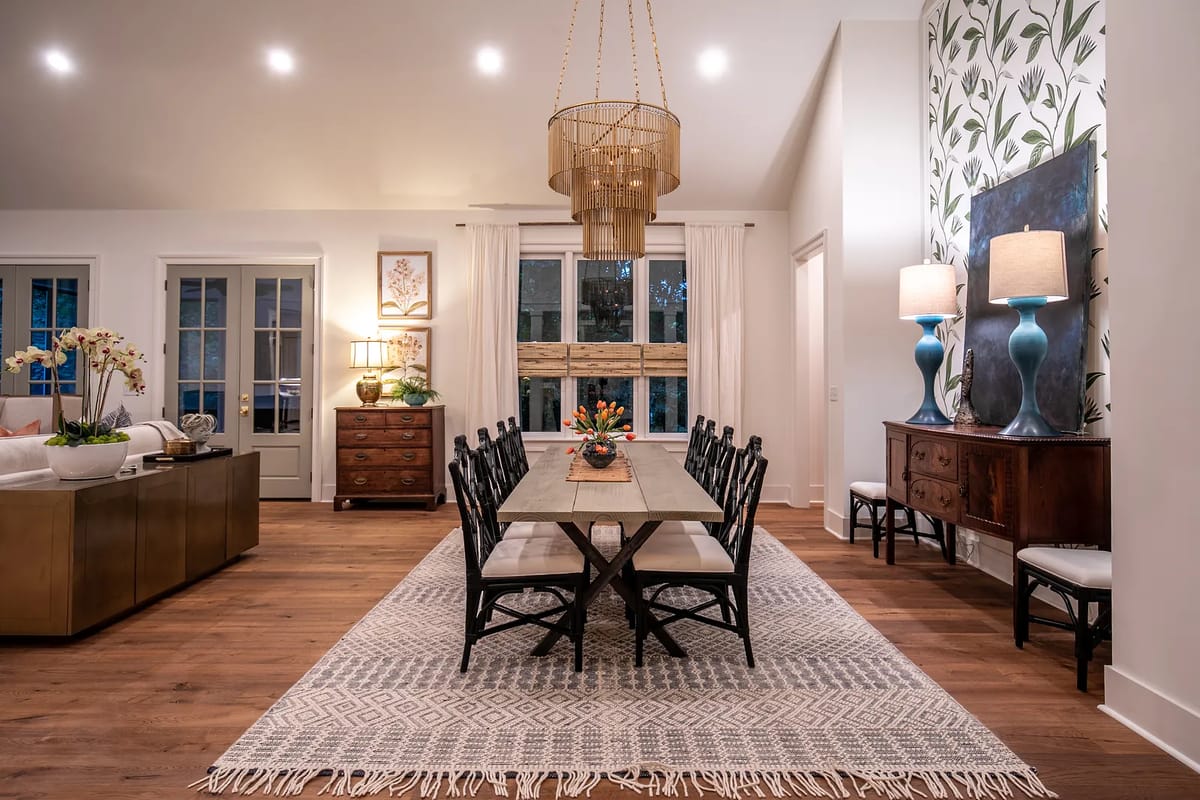 Dining room with rectangular table, black chairs, patterned rug, decorative lamps, and sideboard with natural light.