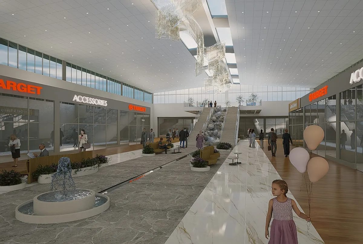 Indoor shopping area with water fountain, escalators, store fronts, planters, benches, and high ceilings.