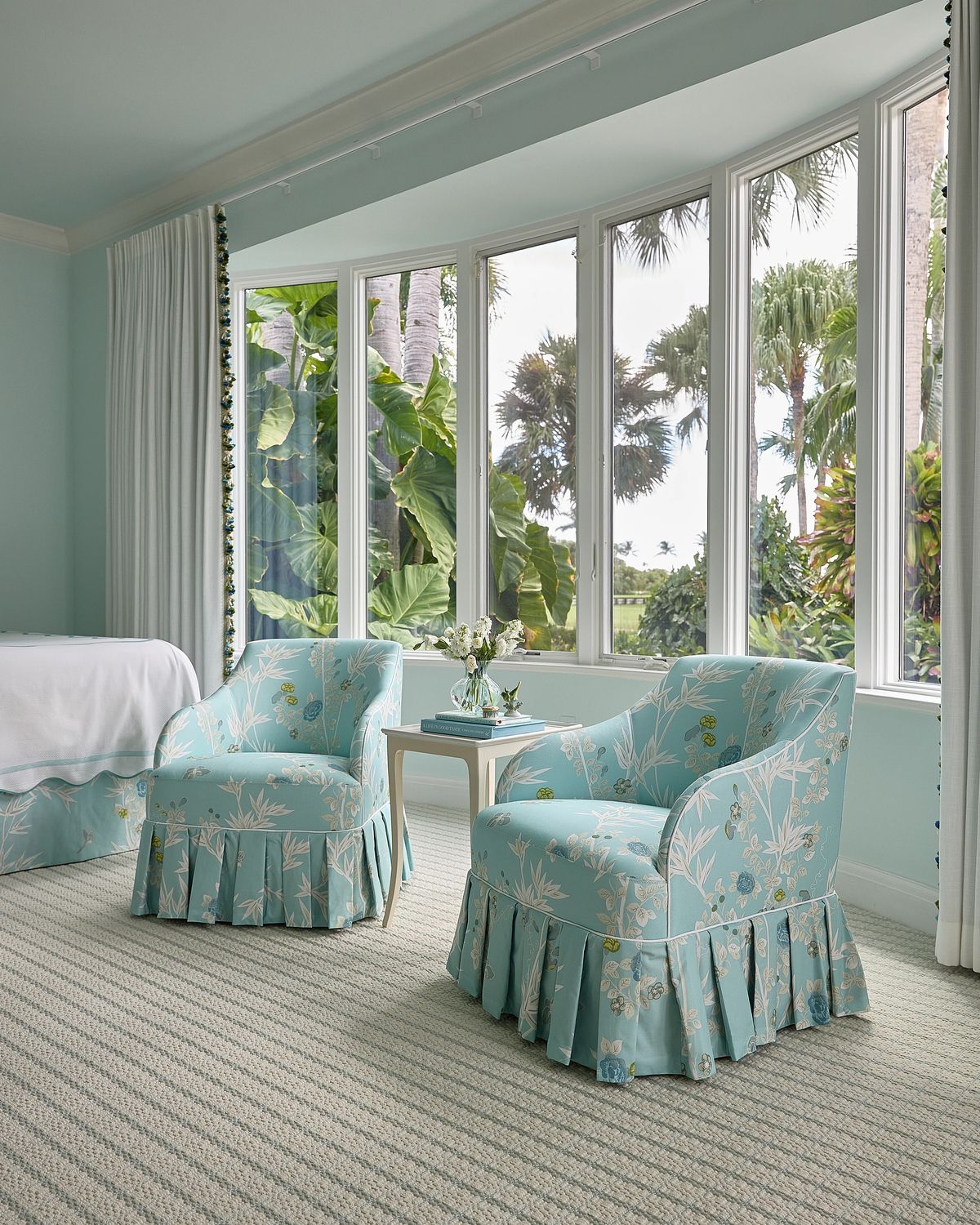 Living room with floral chairs, side table, large windows, and soft blue walls.