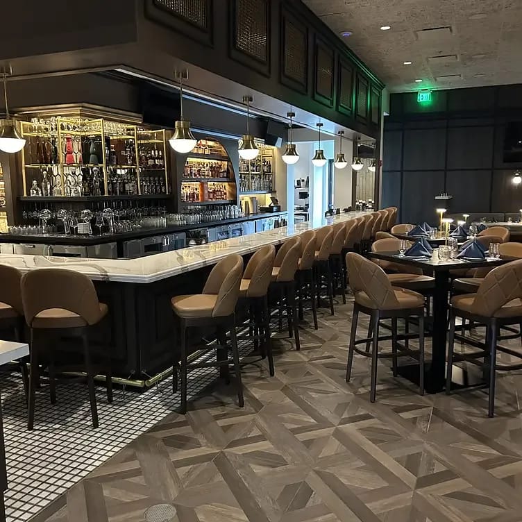 Dining room with bar seating, marble-topped bar, geometric tile floor, tables, and pendant lights.