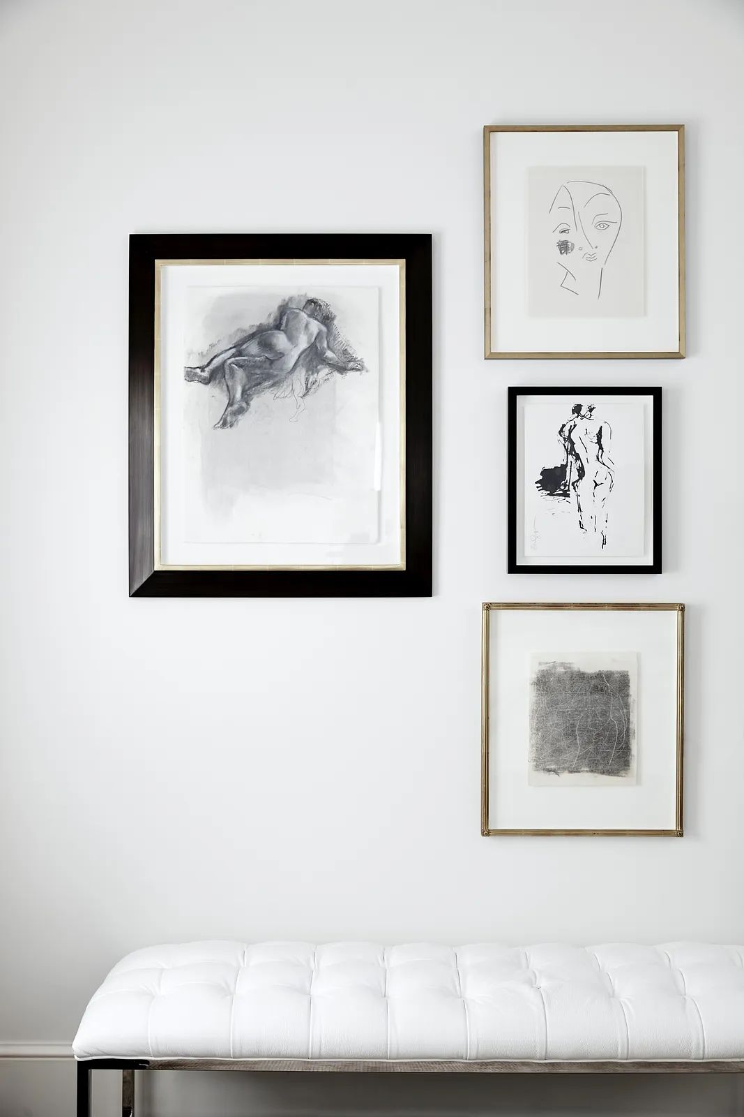 Wall with four framed artworks and a tufted white bench below it.