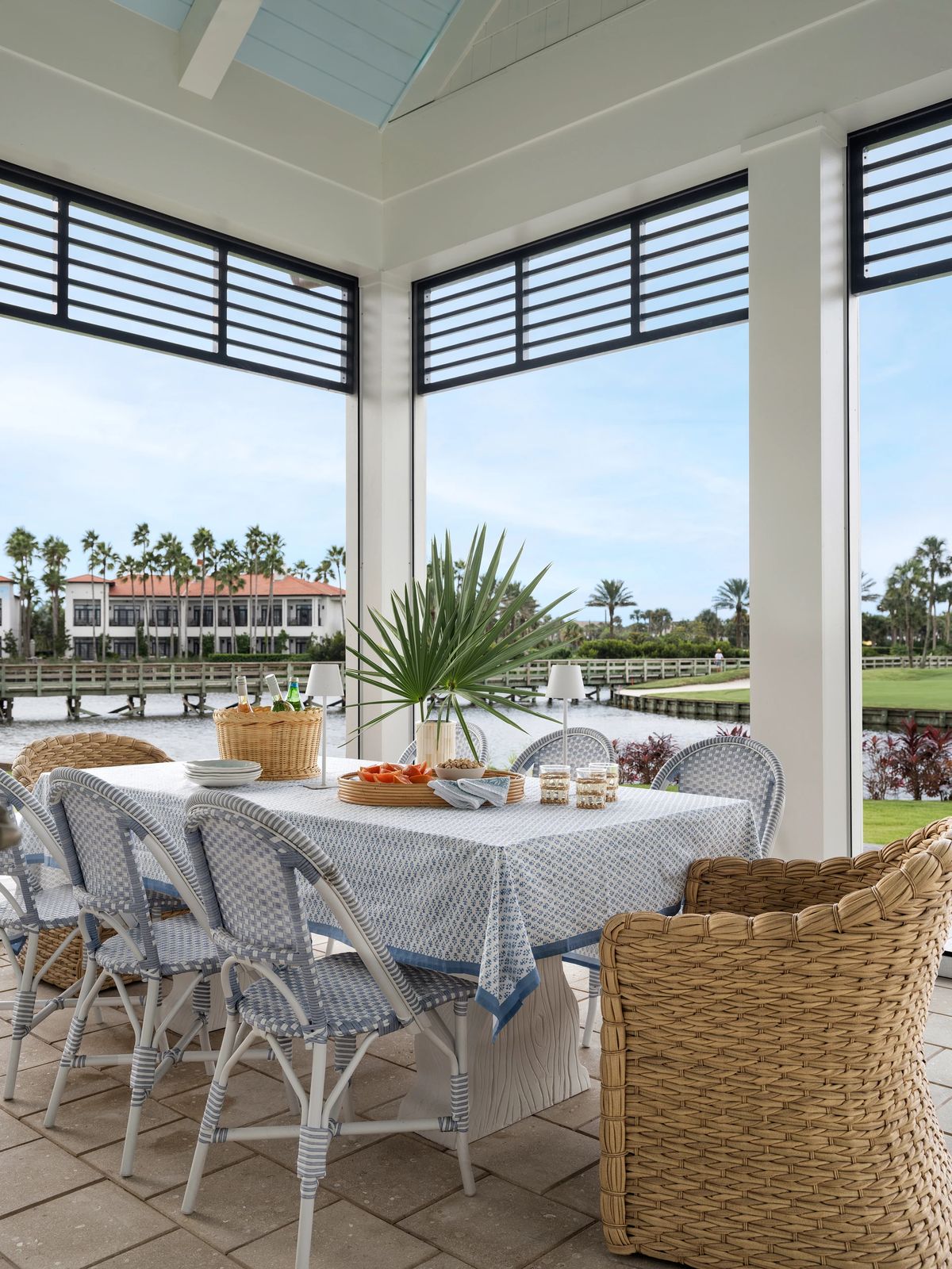 Patio with large table, blue and white striped chairs, woven armchair, fruits, and scenic waterway view