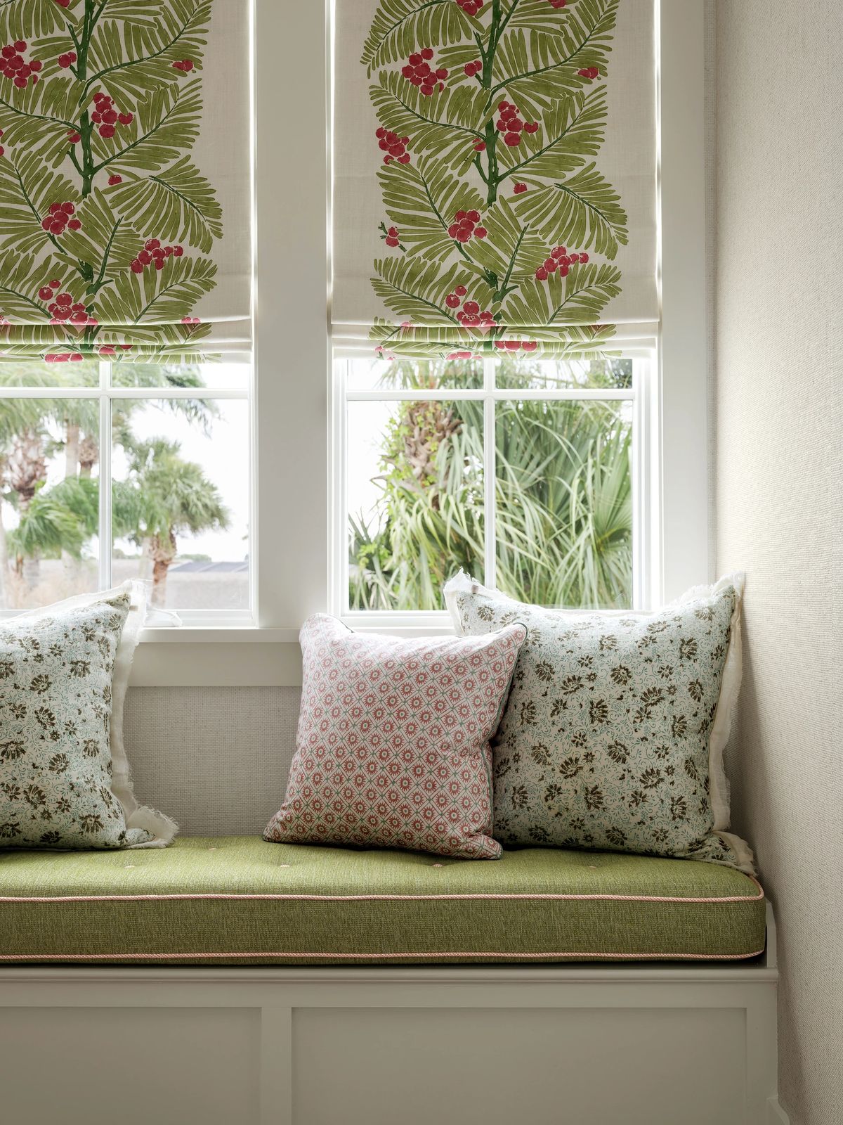 Nook with built-in bench, green cushion, decorative pillows, and patterned blinds covering windows.