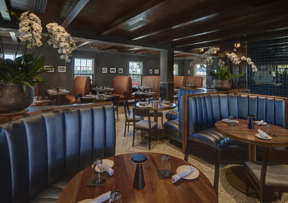 Dining room with navy booths, wooden tables, place settings, plants, and wooden beams.
