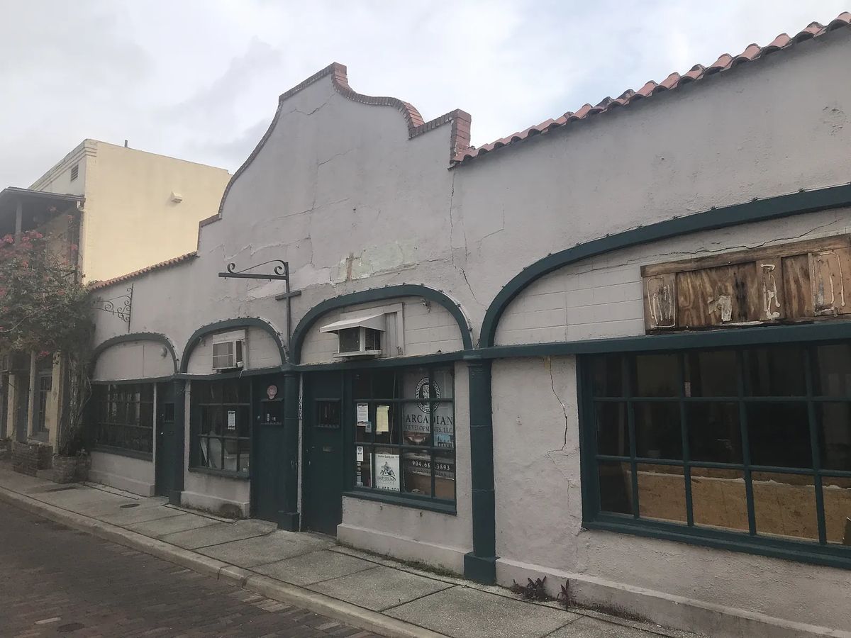 Building facade with stucco walls, arches, large windows, and weathered details.