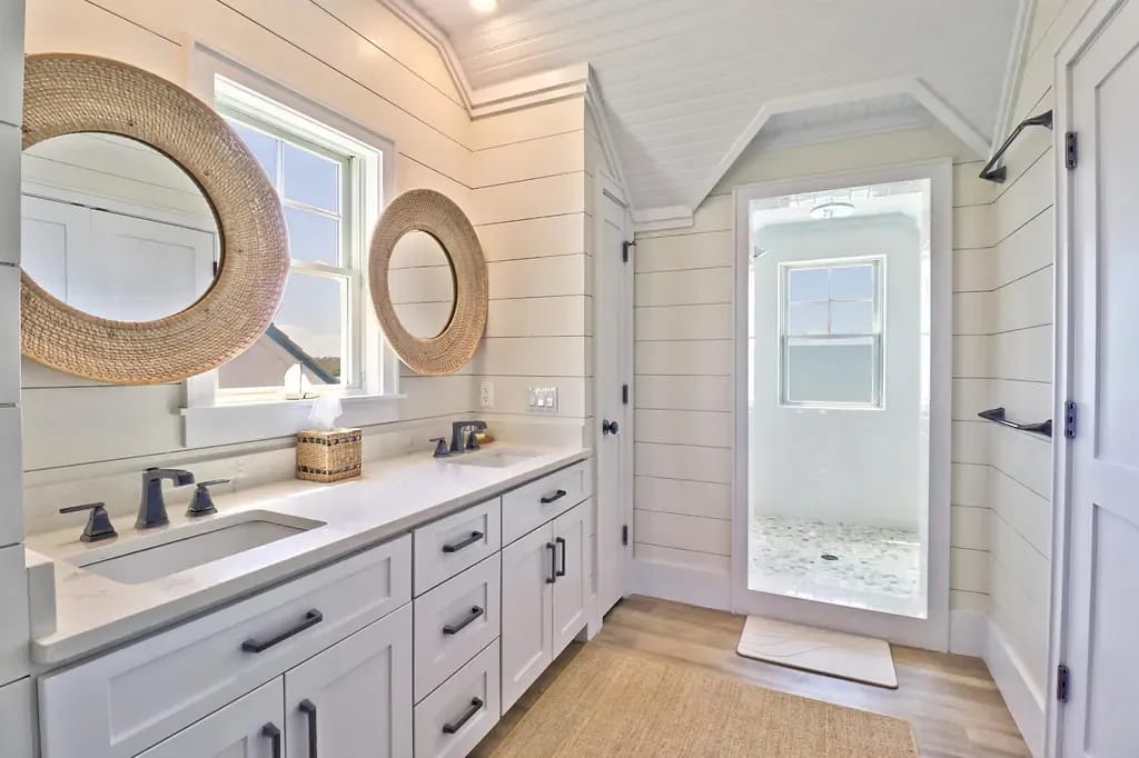 Bathroom with double vanity, round mirrors, dark faucets, shiplap walls, and large shower with glass doors