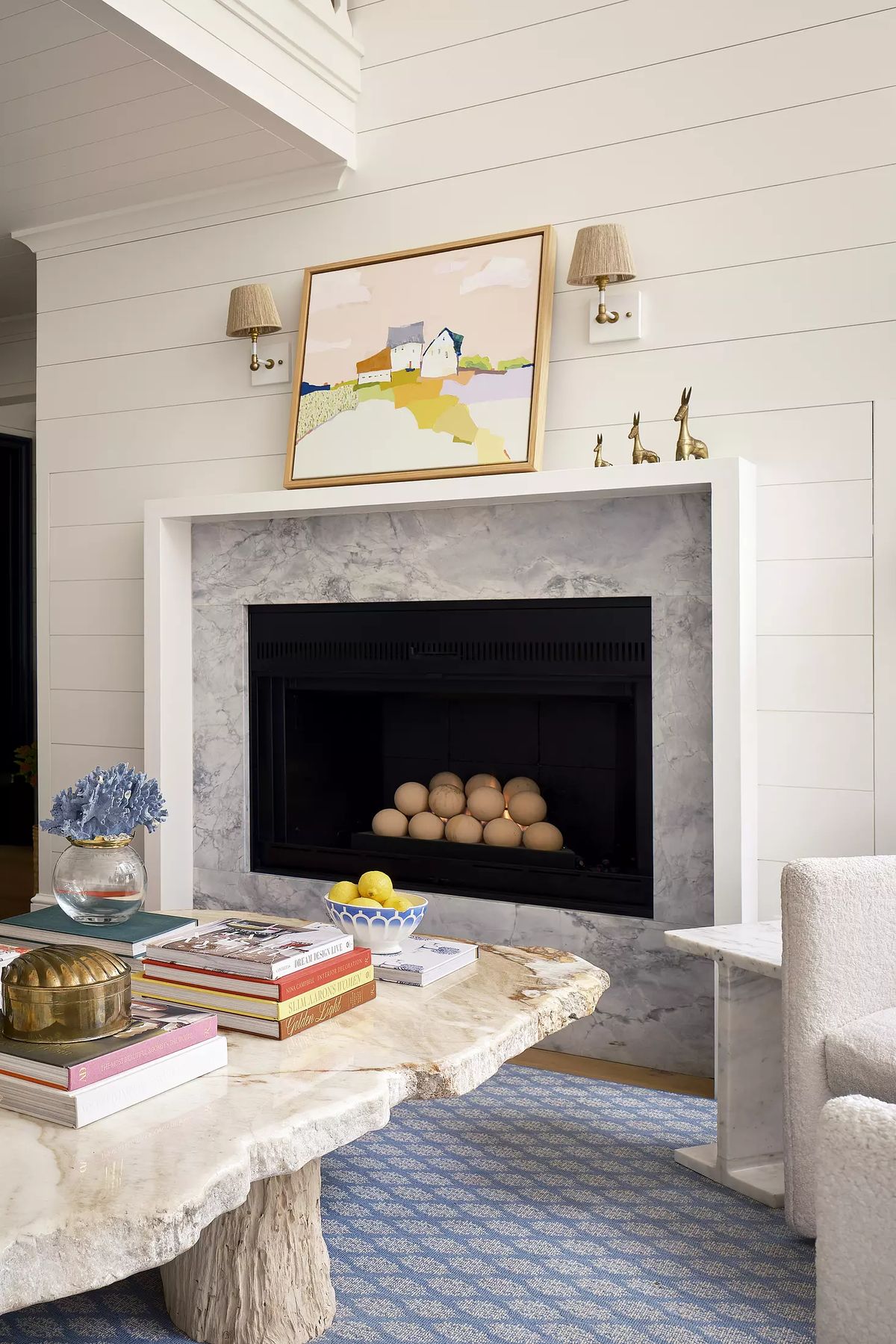 Living room with marble fireplace, abstract painting, stone coffee table, books, bowl with lemons, and blue rug.