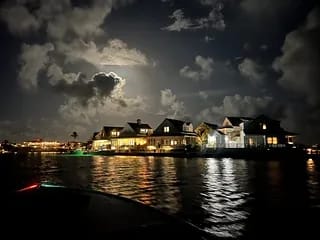 Exterior view of a multi-story waterfront house at night with lights and cloudy sky.