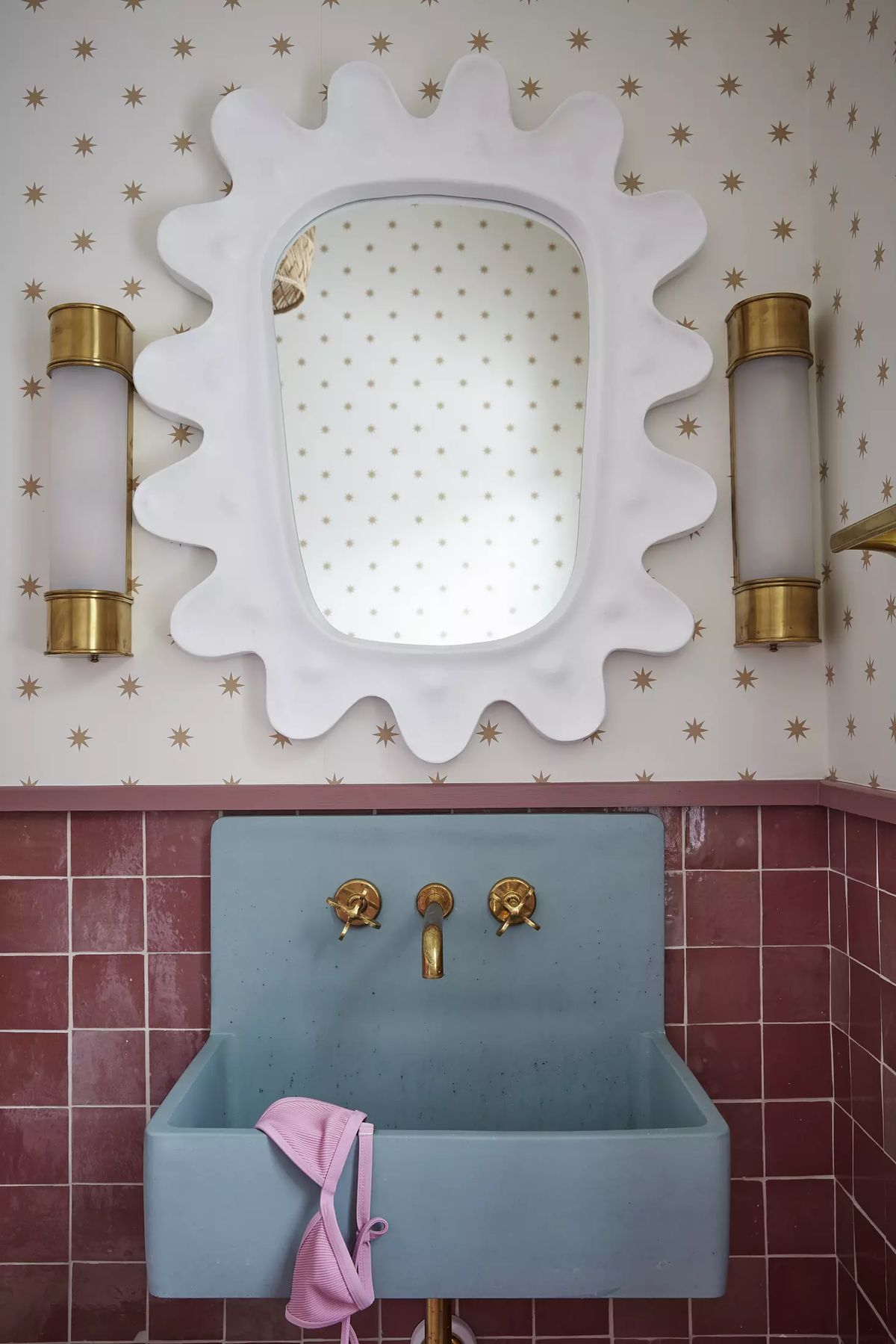 Powder room with blue sink, gold faucets, decorative mirror, star-patterned wallpaper, and pink towel.
