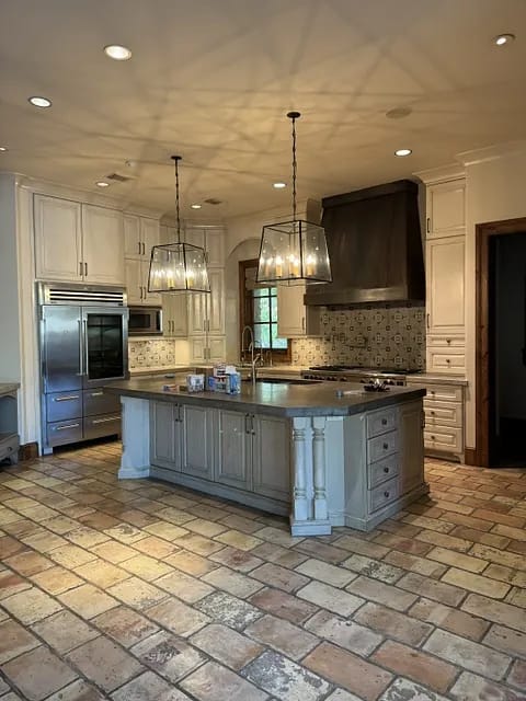 Kitchen with island, gray countertop, wooden cabinets, stainless steel appliances, and tile flooring.