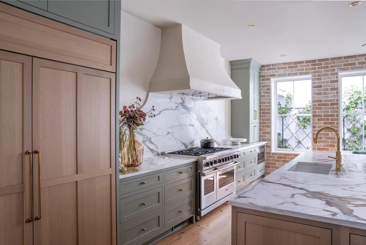 Kitchen with marble countertop, light wood cabinetry, gas range, window, and gold faucet.