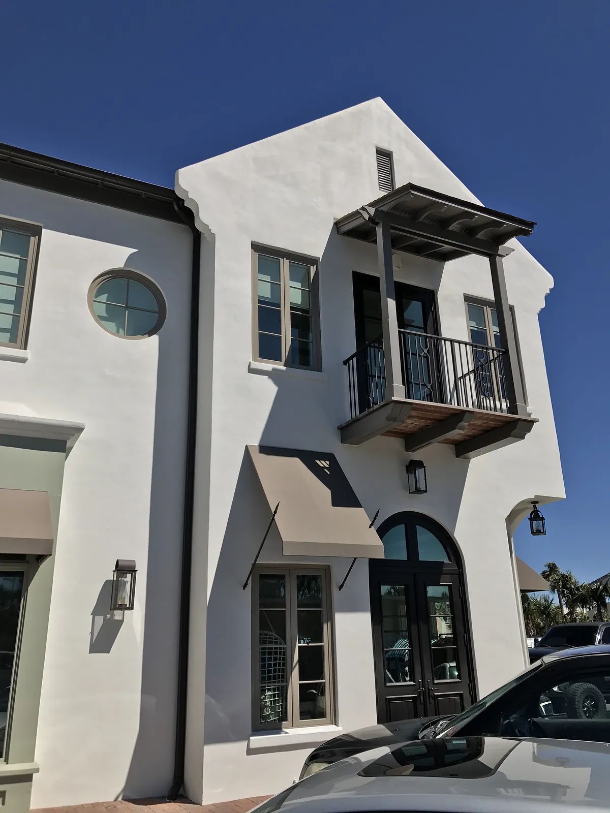 Exterior view of a building with white stucco, balcony, large windows, and decorative awnings.