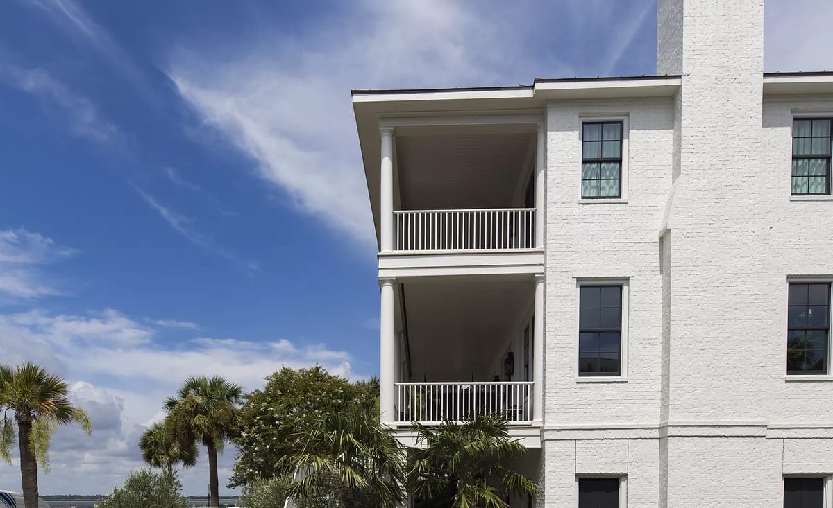 Exterior view of a white brick house with balconies, windows, and palm trees.