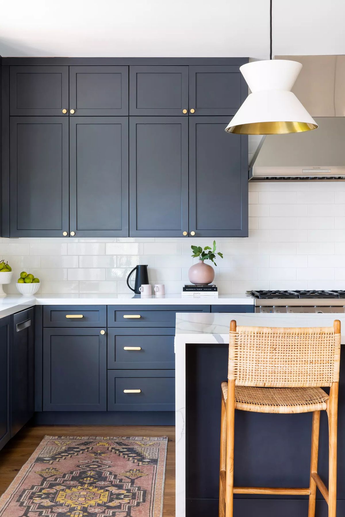 Kitchen with dark blue cabinetry, marble countertop, range hood, bar stool, and patterned area rug