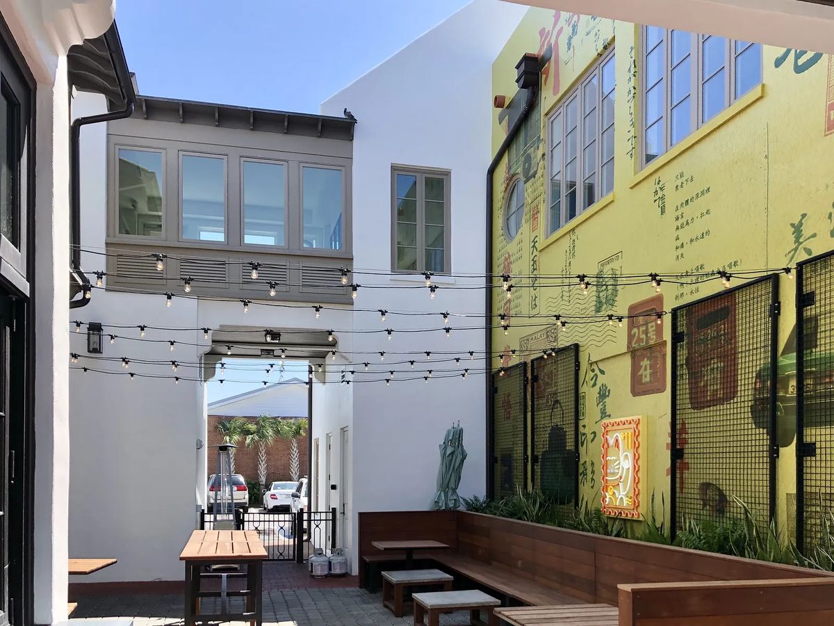Patio with wooden dining table, benches, string lights, and colorful mural.