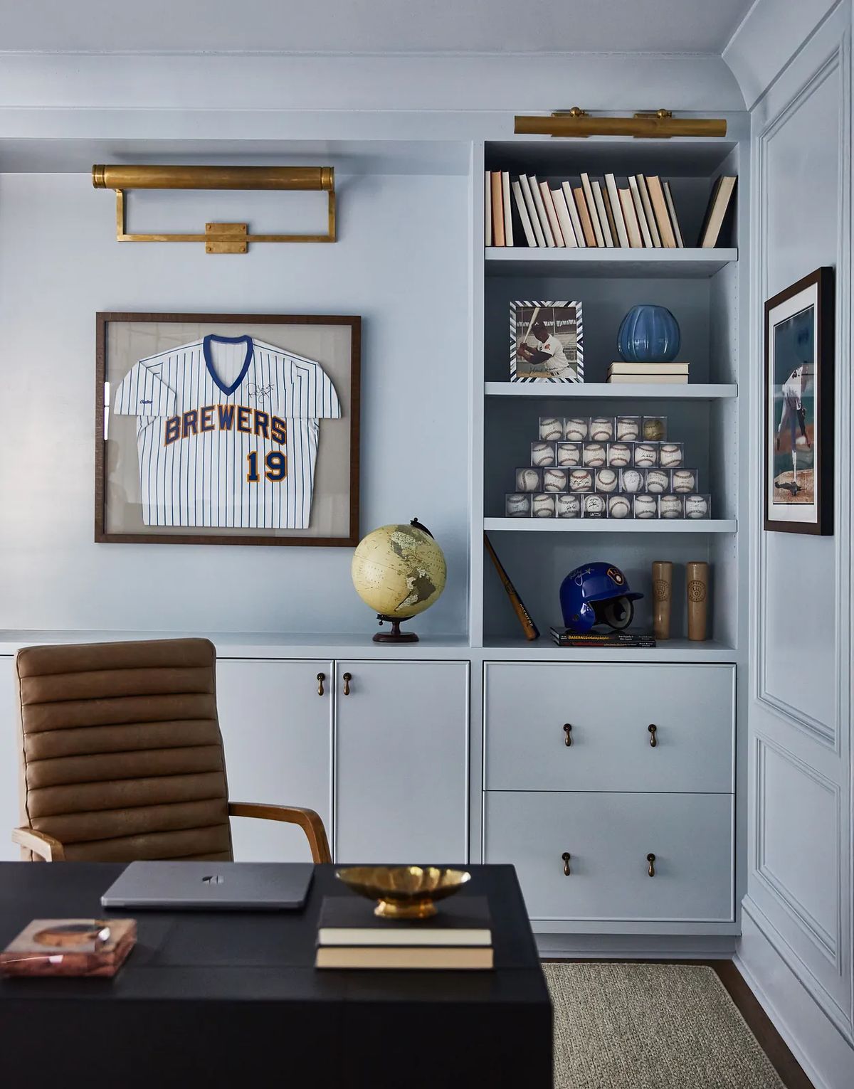 Office with black desk, leather chair, bookshelves, framed artwork, globe, and baseball jersey