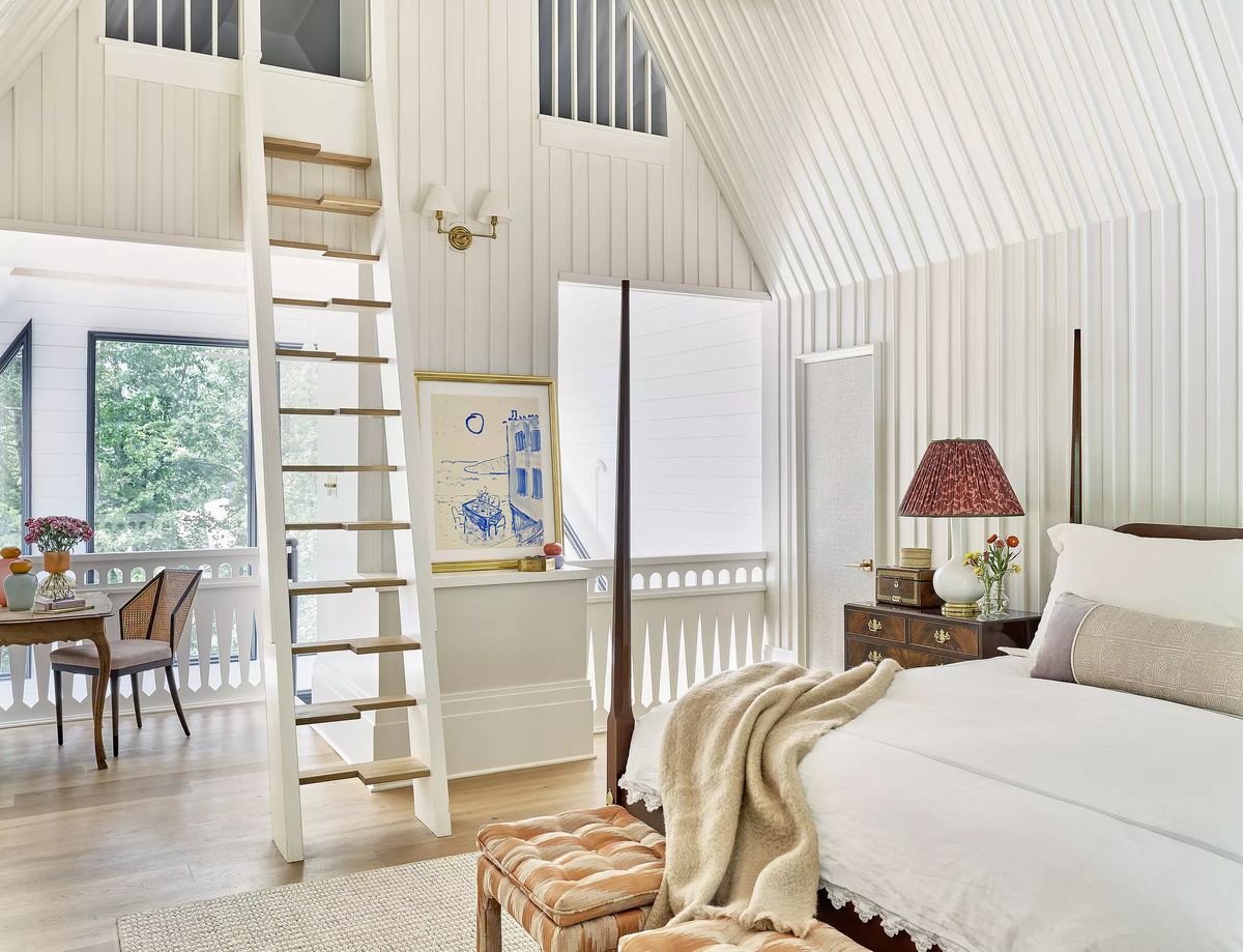Bedroom with bed, nightstand, staircase, large windows, and dining table in the background