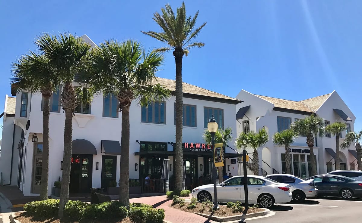 Commercial exterior with two styles, large windows, palm trees, and parked cars.