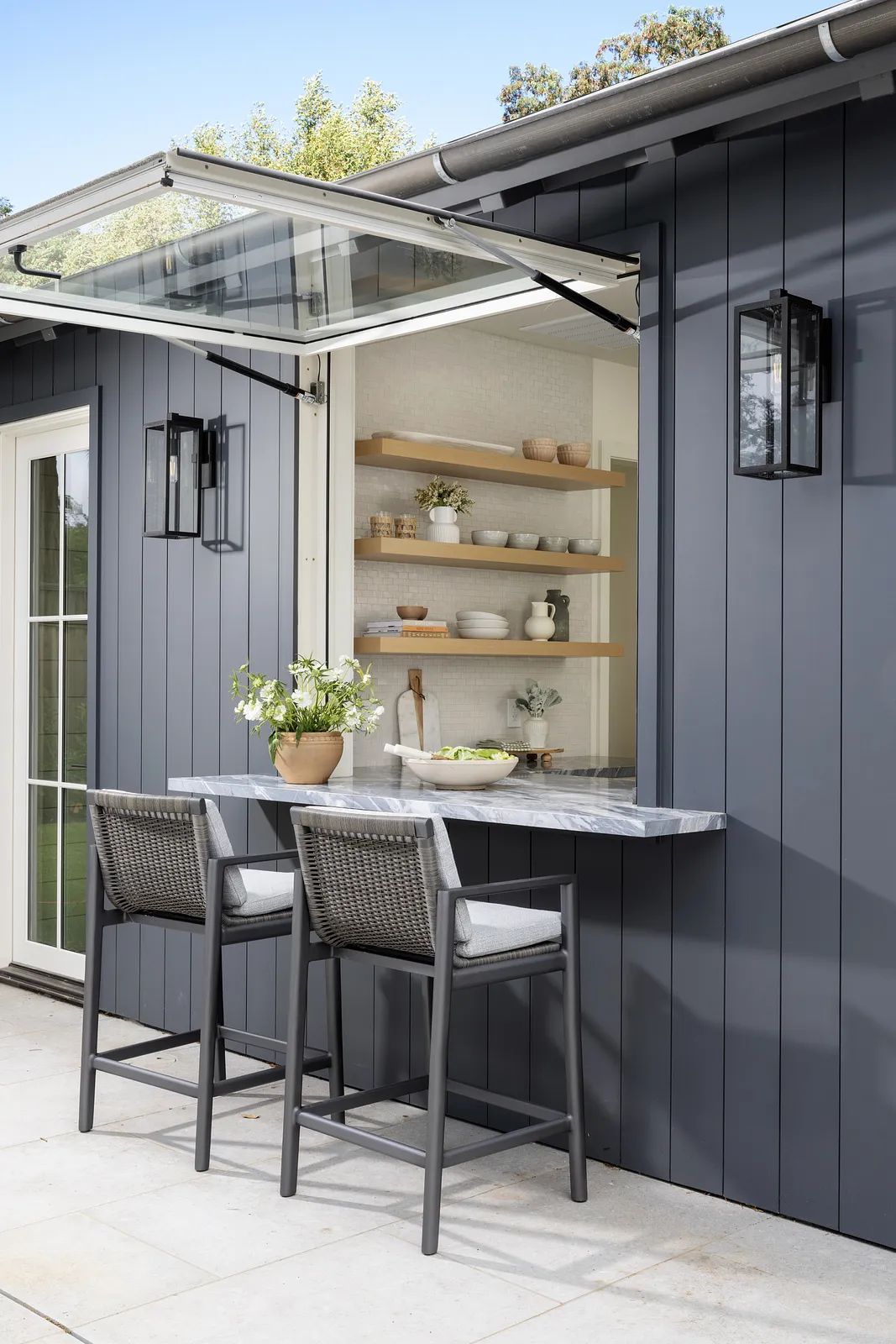 Patio with marble countertop, barstools, wall-mounted shelves, and gray paneled wall with sconces.