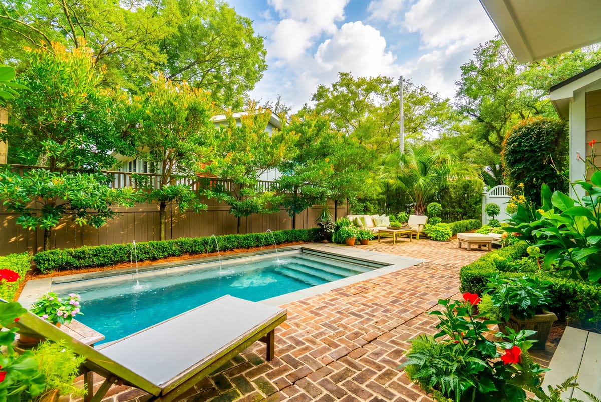 Garden with pool, brick paving, chaise lounges, and lush greenery.