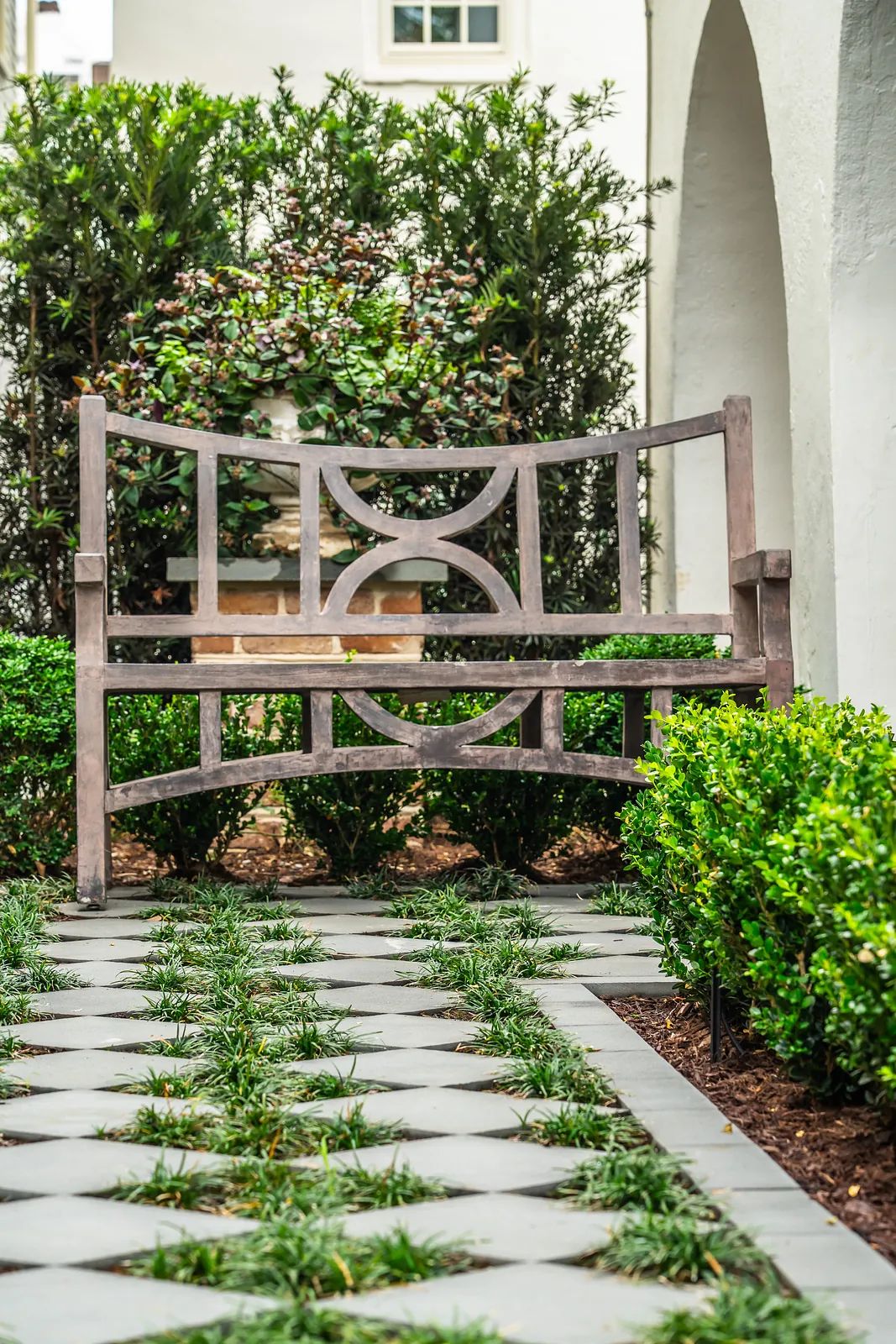 Garden path with decorative bench, low greenery, and structured paver layout.
