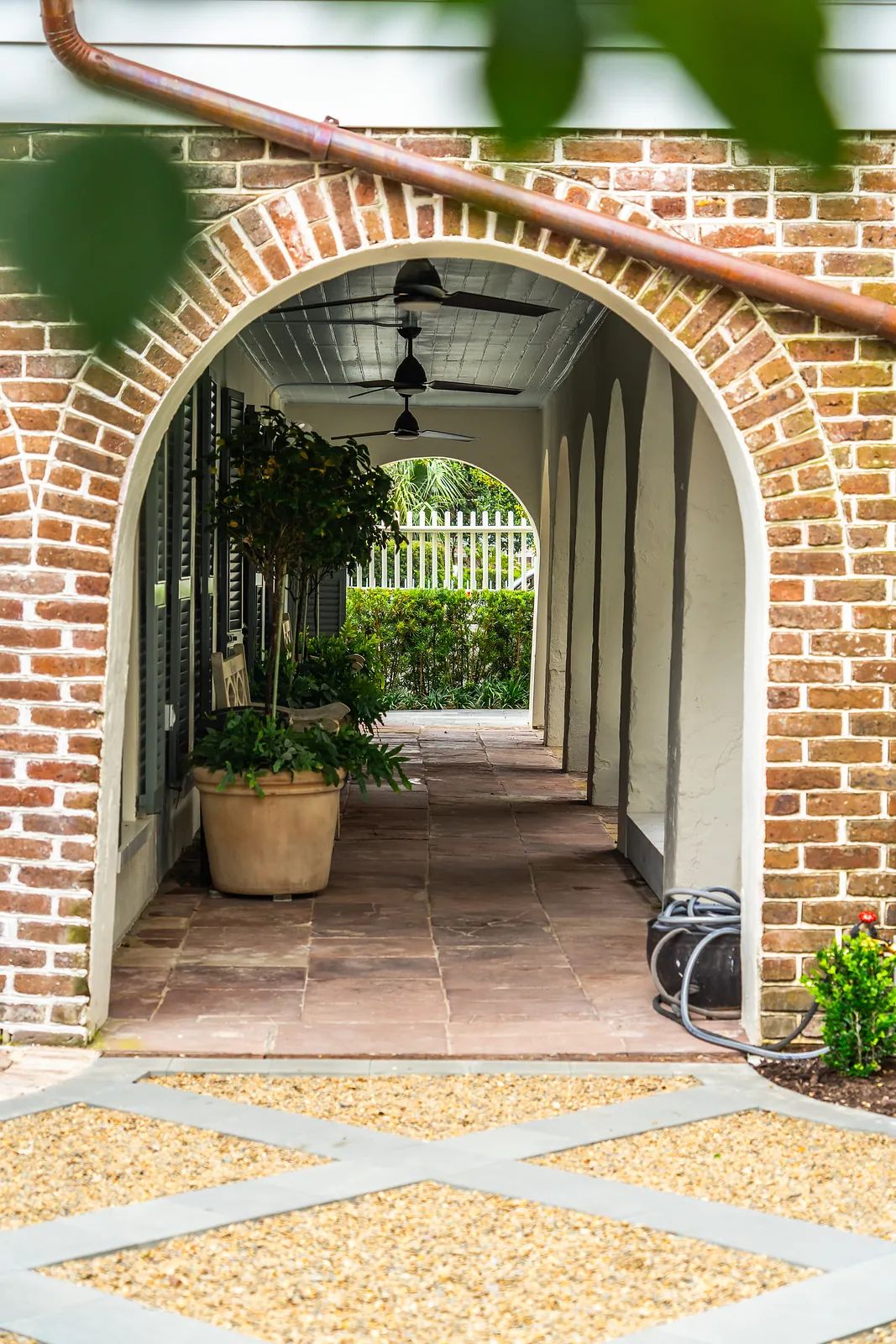 Hallway with arched brick walls, concrete floor, potted plants, and pendant lights.