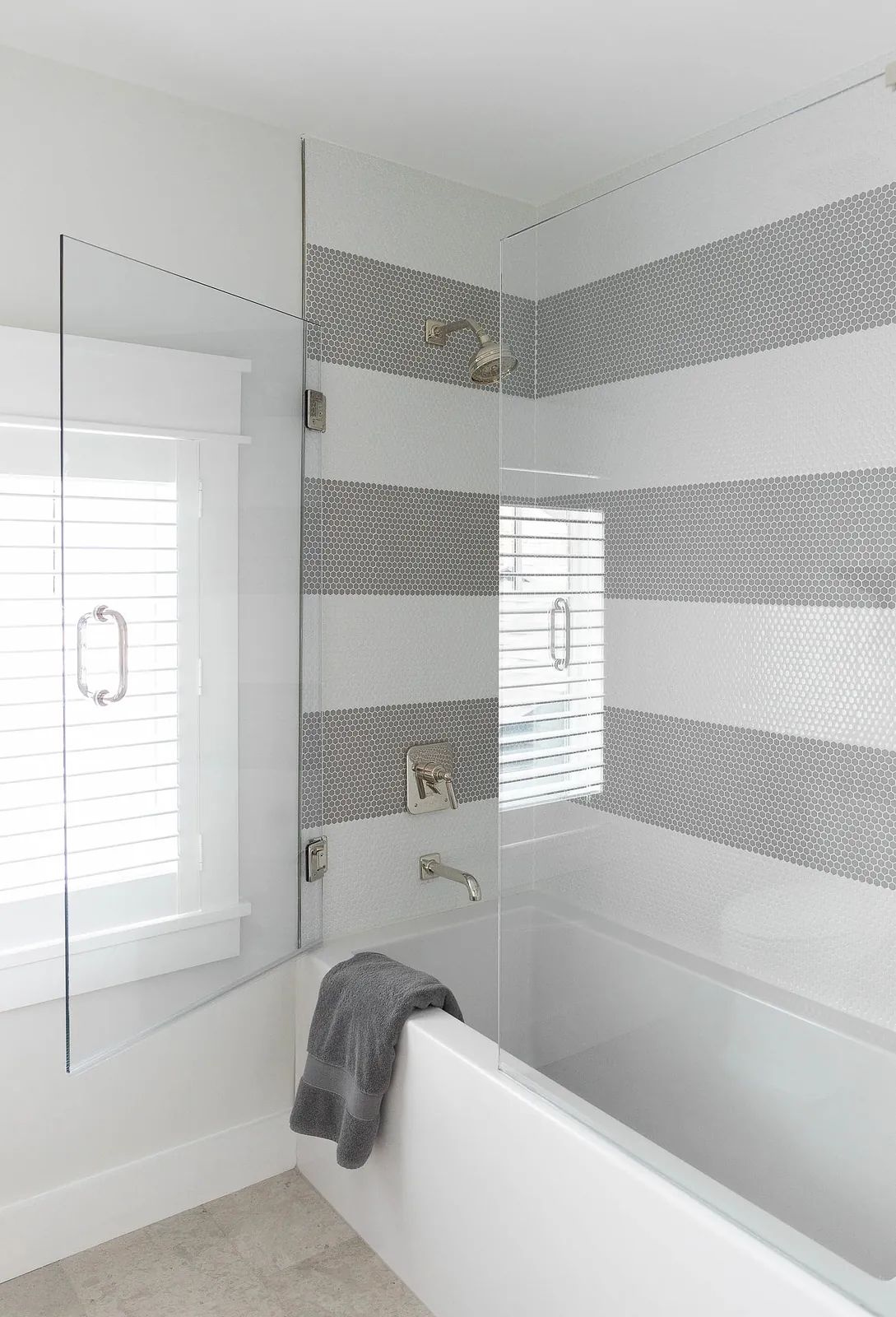 Bathroom with freestanding tub, glass shower enclosure, gray and white striped tiles, and white window.