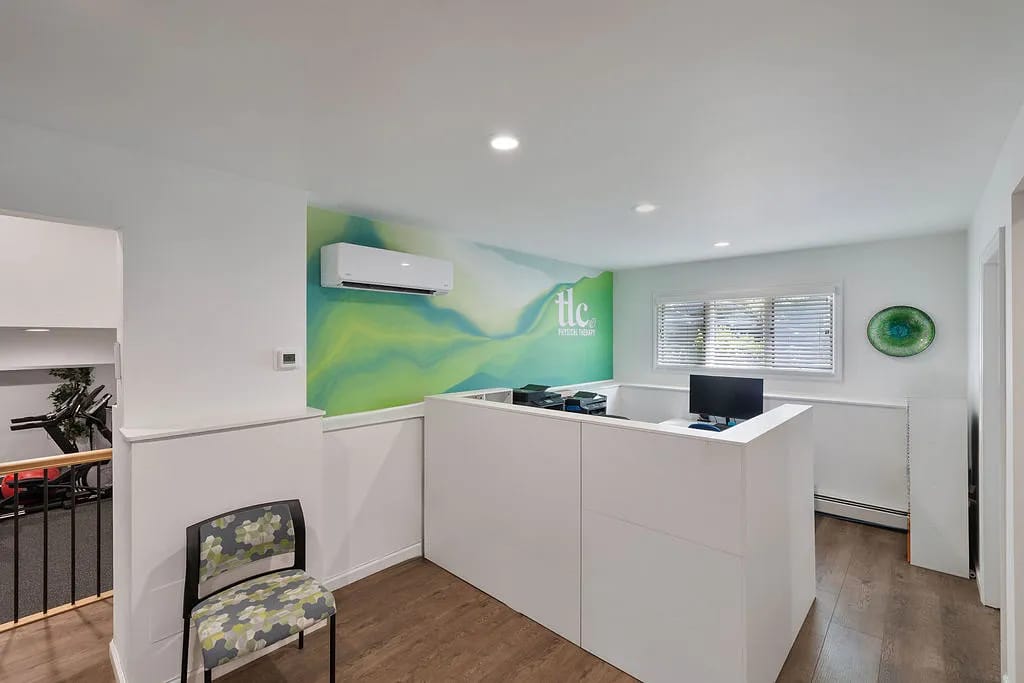Office with computer desk, folding chair, decorative wall, and windows with white blinds.