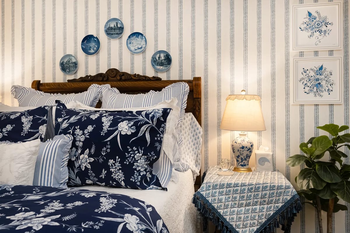 Bedroom with wooden headboard, blue floral bedding, striped wallpaper, and decorative plates.