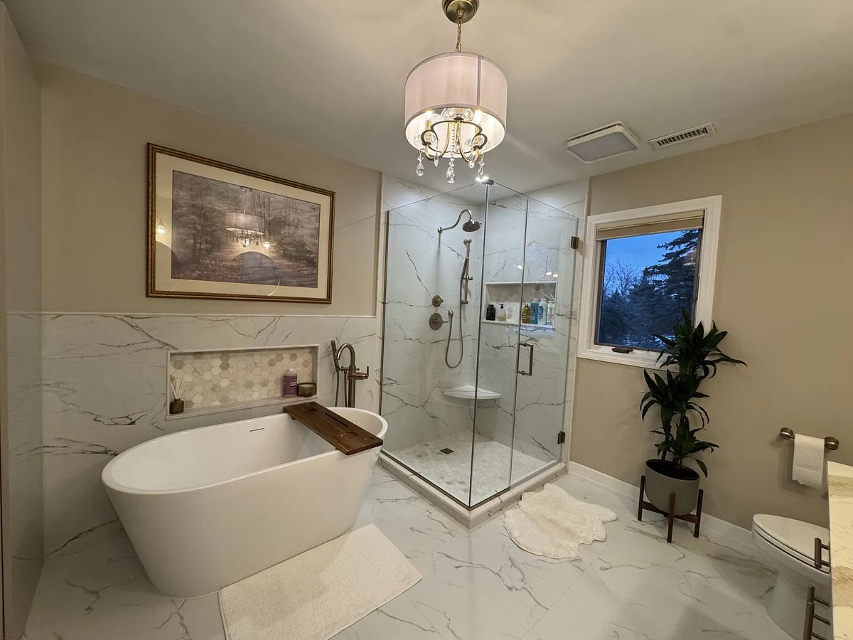 Bathroom with freestanding tub, glass shower, marble tiles, and plant.