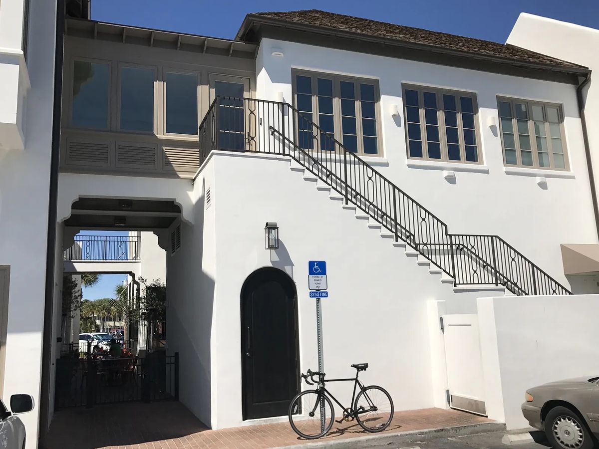 Exterior front view with staircase, large windows, black door, bicycle, and accessible parking sign.