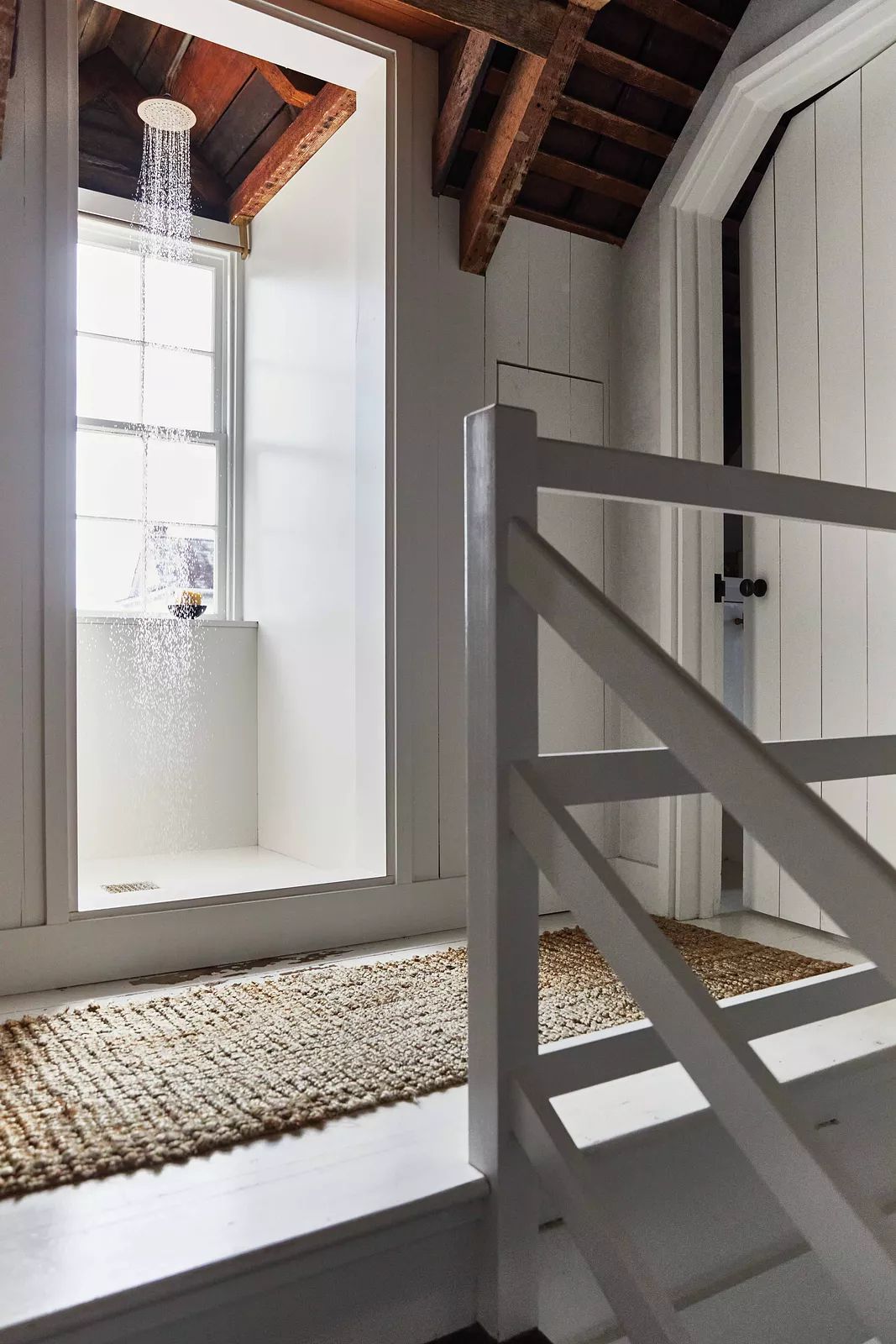 Bathroom with shower, window, woven rug, wooden staircase, white paneling, and exposed beams