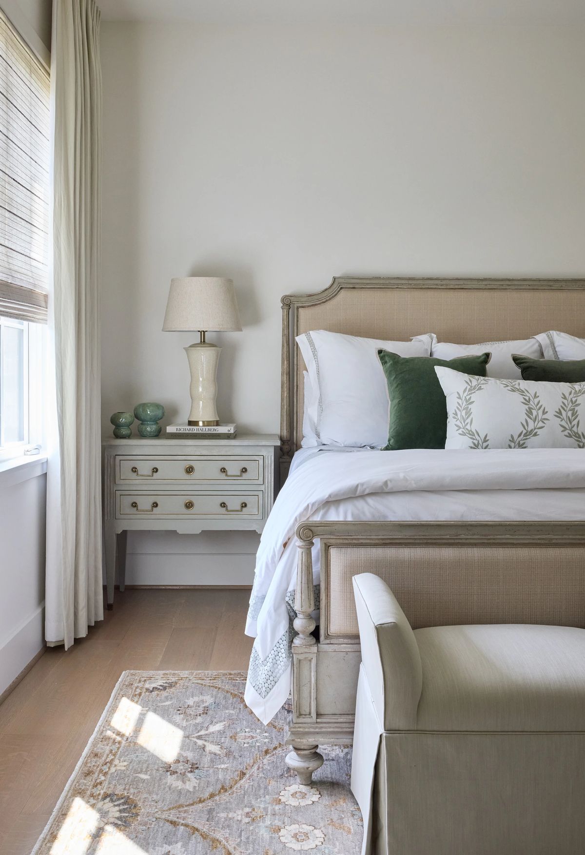 Bedroom with light headboard bed, white bedding, nightstand, lamp, and patterned rug.