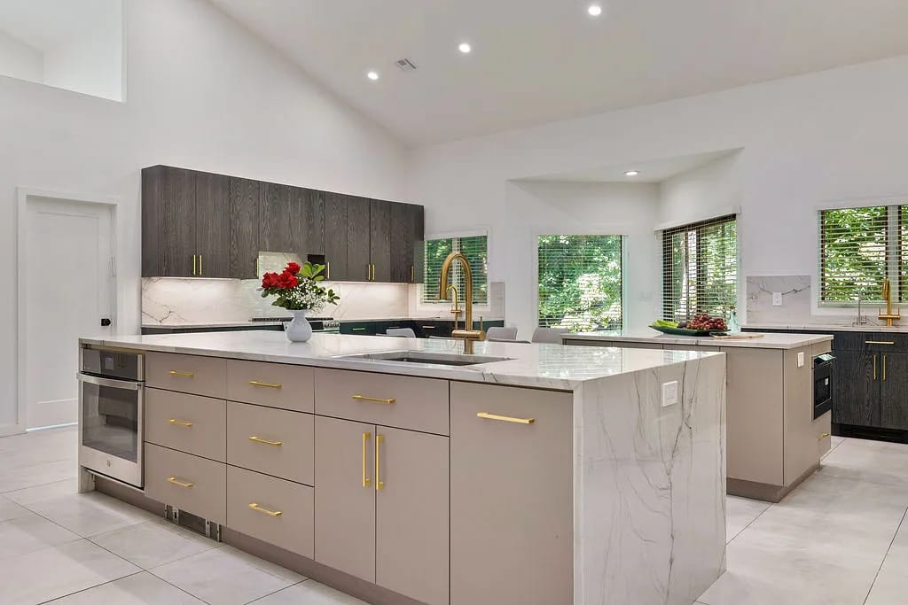 Kitchen with marble island, beige and dark wood cabinets, built-in appliances, and natural light from windows.