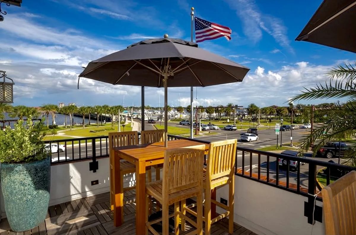 Deck with wooden table, chairs, umbrella, potted plant, views of palm trees and waterfront