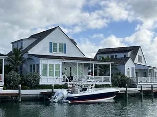 Waterfront view of two white houses with porches and a docked boat.