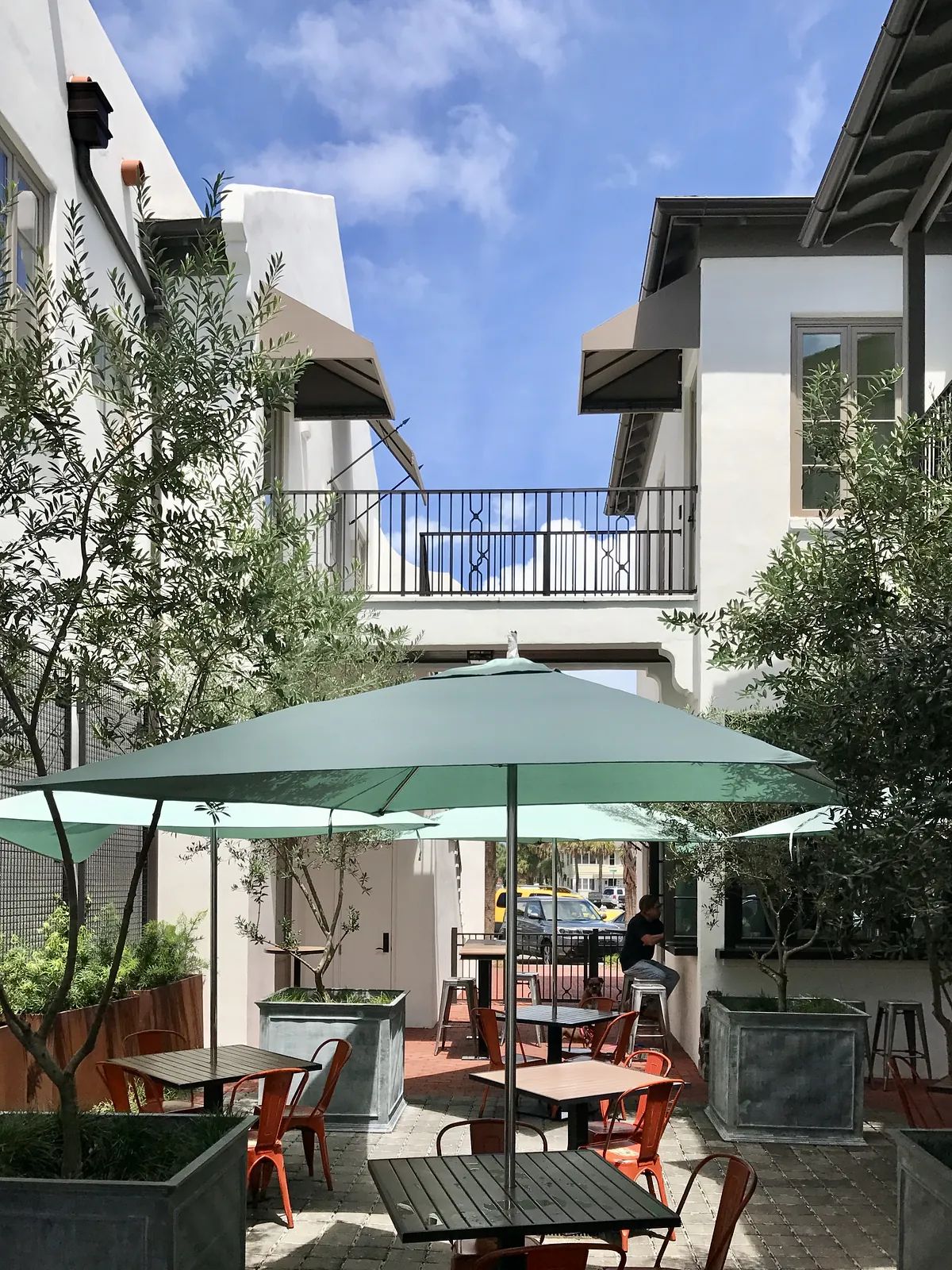 Outdoor patio with green umbrella, metal chairs, tables, and planters.